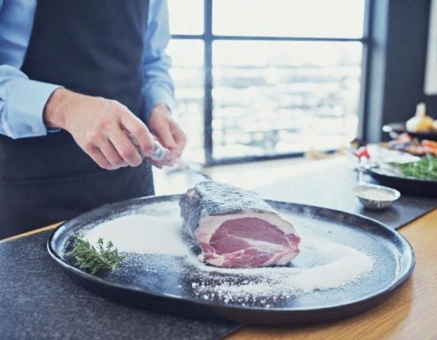 Een chef-kok bestrooit een groot stuk vlees met zout op een schaal.